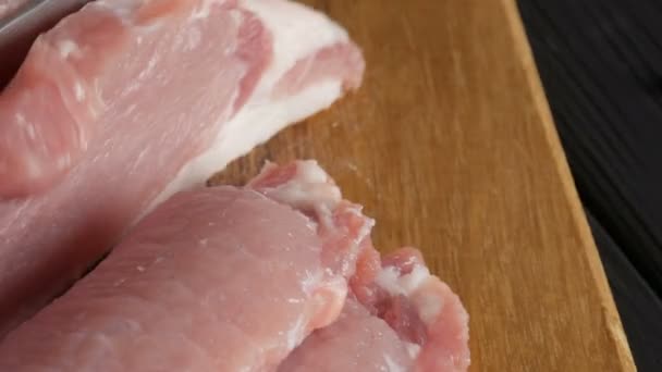 Vista de cerca de las manos femeninas de un cocinero cortado trozos frescos de carne de tocino de cerdo en un tablero de cocina de madera en estilo rústico con un cuchillo de cocina grande — Vídeos de Stock