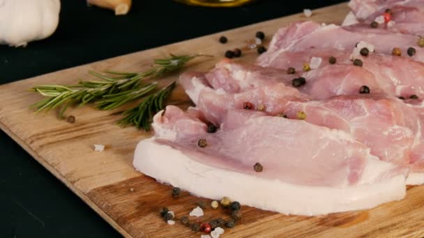 Verse plakjes varkensvlees op een houten keukenbord in rustieke stijl. Knoflook, rozemarijn, grof zout, peper, olijfolie. Huisgemaakt koken. — Stockvideo