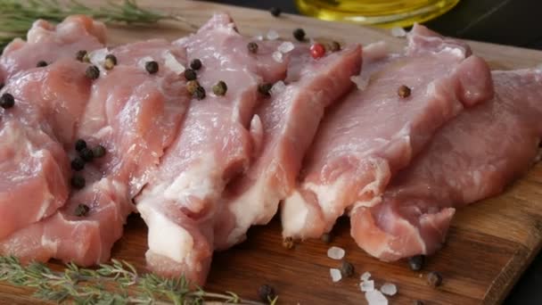 Fresh large pink piece of bacon pork meat on a cutting board of home cooking in a rustic style decorated with black and red pepper and coarse salt — Stock Video