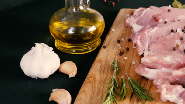 Färska skivor fläskbacon kött på en trä köksbord i rustik stil. Vitlök, rosmarin, grovt salt, peppar, olivolja. Hemlagad matlagning. — Stockvideo