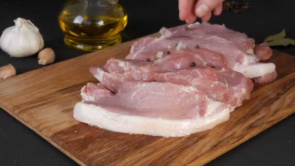 As mãos femininas de um chef decoram com sal grosso, pimenta e alecrim pedaços frescos de carne de bacon de porco em uma placa de cozinha de madeira em um estilo rústico — Vídeo de Stock