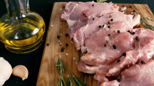 Verse plakjes varkensvlees op een houten keukenbord in rustieke stijl. Knoflook, rozemarijn, grof zout, peper, olijfolie. Huisgemaakt koken. — Stockvideo