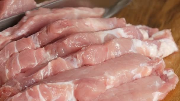 Close-up zicht op de vrouwelijke handen van een kok gesneden verse stukken varkensvlees op een houten keukenbord in rustieke stijl met een groot keukenmes — Stockvideo
