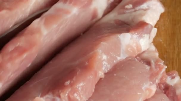 Visão de perto das mãos femininas de um cozinheiro corte pedaços frescos de carne de bacon de porco em uma placa de cozinha de madeira em estilo rústico com uma grande faca de cozinha — Vídeo de Stock