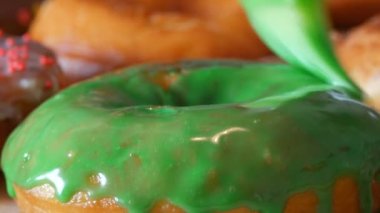 Bir sıra büyük yuvarlak taze kızarmış çörekler bir ev yemeği masasında. Özel bir mutfak silikon fırçası çöreğin yüzeyine parlak yeşil bir jöle sürer. Yağlı, abur cubur, fast food. Yaklaş.