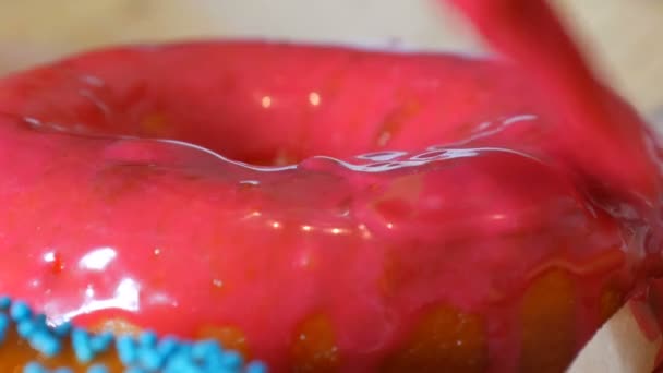 Una fila de rosquillas redondas más grandes recién fritas en una mesa de cocina casera. Un cepillo especial de silicona de cocina aplica un esmalte rosa brillante a la superficie de la dona. Grasa, comida chatarra, comida rápida de cerca — Vídeos de Stock