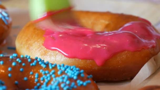 Een rij grotere ronde vers gebakken donuts op een zelfgemaakte kooktafel. Een speciale keuken siliconen borstel brengt een felroze glazuur aan op het oppervlak van de donut. Vet, junkfood, fastfood — Stockvideo