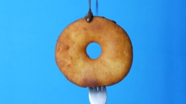 Üzerinde çikolata kreması ve mavi tozun mavi arka planda döndüğü bir çatalda büyük yuvarlak bir çörek.