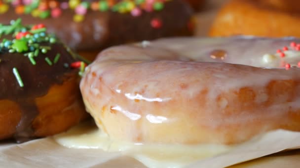 Os grandes donuts fritos frescos multicores sucessivamente em uma mesa. Um belo donut com cobertura branca é polvilhado com um pó colorido especial para decoração de doces. — Vídeo de Stock