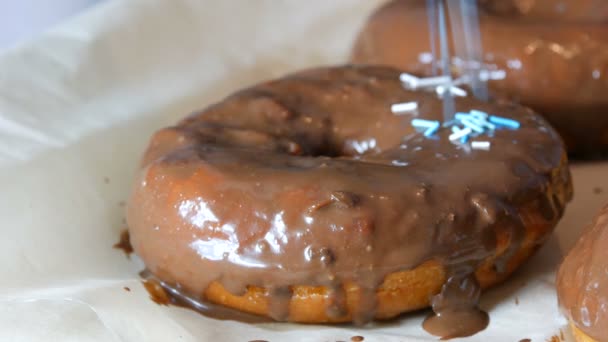 Las rosquillas grandes fritas frescas multicolores en una fila sobre una mesa. Una hermosa dona con glaseado de chocolate se rocía con un polvo de color especial para la decoración de dulces — Vídeos de Stock