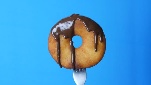Großer runder Donut auf einer Gabel, auf der Schokoglasur auf blauem Hintergrund fließt — Stockvideo