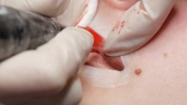 Mikro patenli dudak dövmesi ve kozmetoloji kliniğindeki dudak rengini düzelten kırmızı pigment. Kalıcı makyaj dudakları prosedürü. Dövme makinesiyle dudaklara pigment makyaj uygulanıyor.