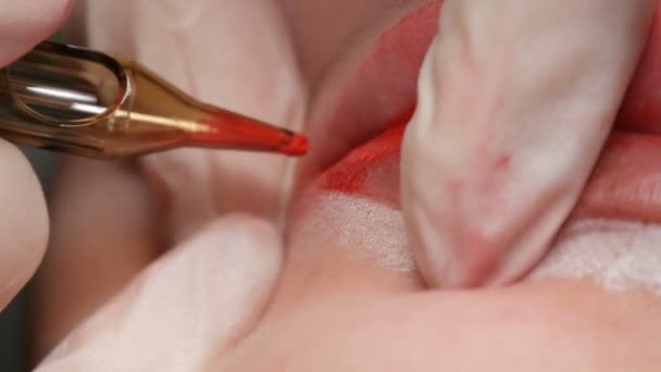 Tatuaje de labio Microblading con un pigmento rojo colorante especial que corrige el color de los labios en una clínica de cosmetología. Procedimiento permanente de los labios del maquillaje que aplica el maquillaje del pigmento en labios con una máquina del tatuaje — Vídeo de stock