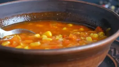 Sıcak kaynamış kırmızı domates çorbası ve mısır. Kahverengi kil tabaktaki bir kaşıkla karıştırılır.