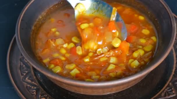 Horká pouze vařená červená rajčatová polévka s kukuřicí, která je smíchána se lžící v hnědém hliněném talíři v rustikálním stylu — Stock video