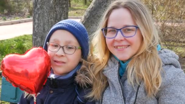 Retrato de mamá divertida y su hijo adolescente niño en gafas, sonriendo en la primavera en el parque. Día de las madres, felicitaciones, globo en forma de corazón . — Vídeos de Stock