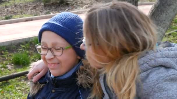 Grappige moeder en haar kleine tiener in een bril, glimlachend in de lente in het park. Moederdag groet, moeder kust haar kind. — Stockvideo