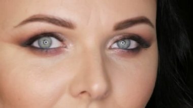 Parlak makyajlı, mavi gözlü, siyah bir arka planda siyah gözlü güzel bir kadının yakın plan portresi.