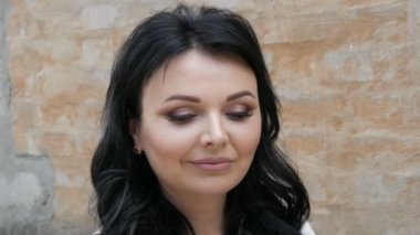 Parlak makyajlı güzel bir genç kadının portresi, dumanlı gözler mavi gözler ve siyah uzun saçlar, arka planda kırmızı bir tuğla duvar.