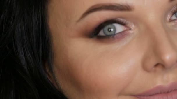 Close-up retrato do rosto de uma bela jovem com maquiagem noite brilhante e olhos azuis, olhos fumegantes fazer em um fundo preto em um estúdio — Vídeo de Stock
