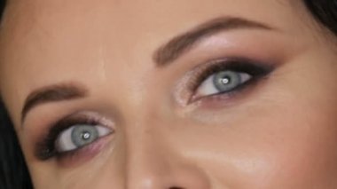 Parlak makyajlı, mavi gözlü, siyah bir arka planda siyah gözlü güzel bir kadının yakın plan portresi.