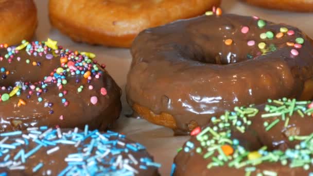 Grandi ciambelle fritte fresche multicolori in fila su un tavolo. Una bella ciambella con glassa al cioccolato è cosparsa di una speciale polvere colorata per la decorazione dei dolci. — Video Stock