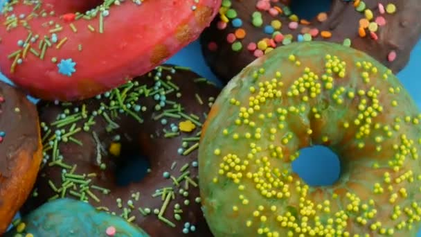 Amerikaanse donuts met kleurrijk glazuur en poeder. Draaien op een blauwe achtergrond van dichtbij bekijken — Stockvideo