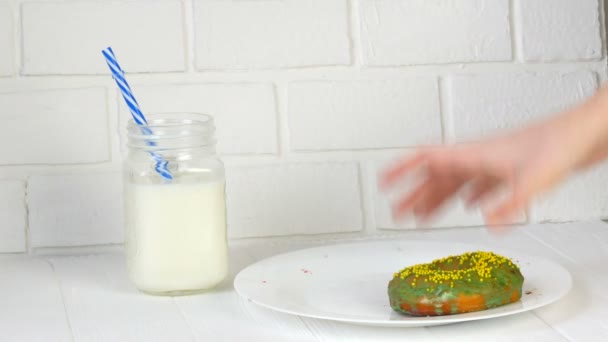 Жіночі руки поклали великий американський пончик з багатокольоровим порошком на задній план білої цегляної стіни і молока в банці. Нездорова їжа, діабет — стокове відео