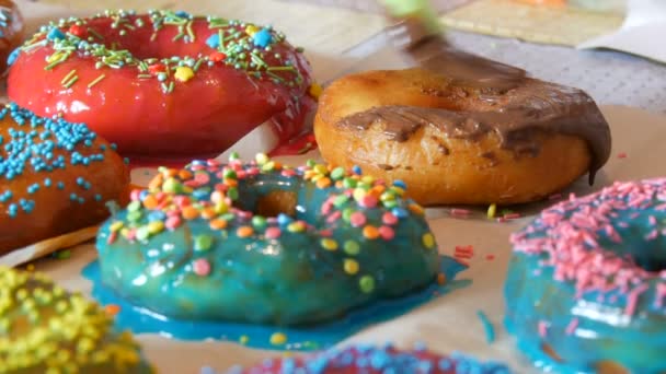Eine Reihe größerer runder, frisch gebratener Donuts auf einem heimischen Kochtisch. Eine spezielle Silikonbürste für die Küche trägt eine helle Schokoladenglasur auf die Oberfläche des Donuts auf. Fettiges, Junk Food, Fast Food aus nächster Nähe — Stockvideo