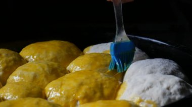 Pişirme tepsisinde ev yapımı pişirme, dişi bir fırıncı hamurun toplarını yumurta sarısı ile yağlıyor. Hamur yağlamak için özel mutfak silikon fırçası. Ukrayna evcil hamur tatlısı