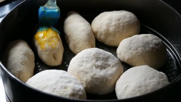 Zelfgemaakt bakken op een bakplaat, een vrouwelijke bakker smeert de ballen van het deeg met eigeel. Speciale siliconen borstel voor het insmeren van deeg. Oekraïense binnenlandse dumplings — Stockvideo