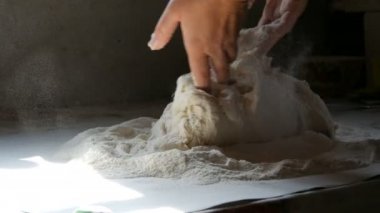 Kadın eli hamuru siyah bir arka planda kırsal bir tarzda yoğurur. Un havada uçuşuyor.