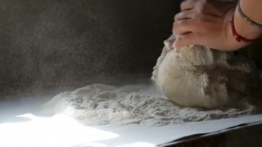 Kadın eli hamuru siyah bir arka planda kırsal bir tarzda yoğurur. Un havada uçuşuyor.