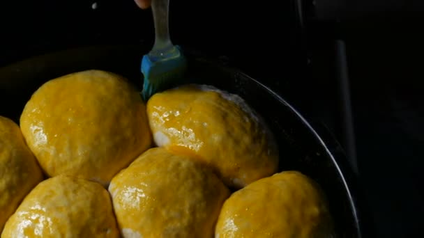 Zelfgemaakt bakken op een bakplaat, een vrouwelijke bakker smeert de ballen van het deeg met eigeel. Speciale siliconen borstel voor het insmeren van deeg. Oekraïense binnenlandse dumplings — Stockvideo