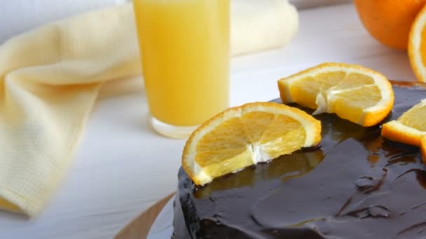 Beyaz bir mutfakta meyve suyunun yanında kremalı ve portakal dilimli ev yapımı çikolatalı pasta. — Stok video
