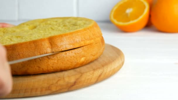Hände einer Bäckerfrau schneiden in der Küche mit einem Messer einen Orangenkeks oder Biskuitteig an. Herstellung von süßen hausgemachten Kuchen. — Stockvideo
