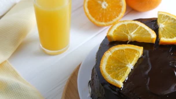 Домашний шоколадный торт с глазурью и апельсиновыми ломтиками рядом с соком на белой кухне — стоковое видео