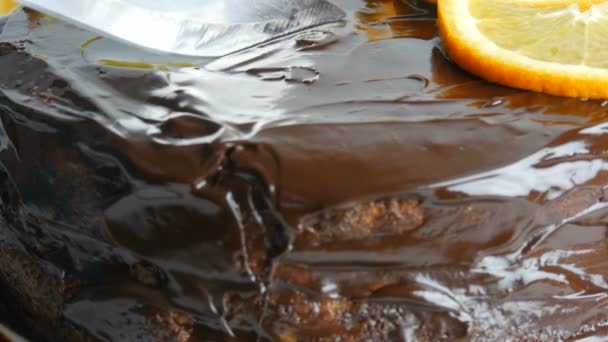 Een mes snijdt een heerlijk koekje. Close-up zicht op zelfgemaakte chocoladetaart met glazuur en sinaasappelschijfjes. Zoet Dieetvoeding. — Stockvideo