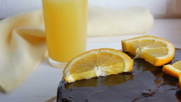 흰 부엌에 있는 주스 옆에 설탕 과 오렌지 조각이 붙어 있는 초콜릿 케이크를 먹는 모습 — 비디오