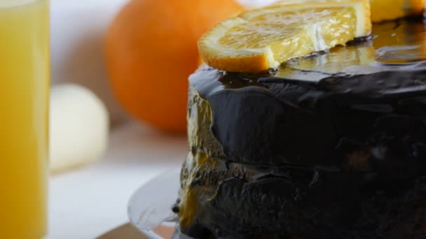 흰 부엌에 있는 주스 옆에 설탕 과 오렌지 조각이 붙어 있는 초콜릿 케이크를 먹는 모습 — 비디오