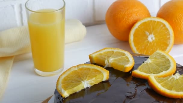 白いキッチンでジュースの横にアイシングとオレンジのスライスと自家製チョコレートケーキ — ストック動画