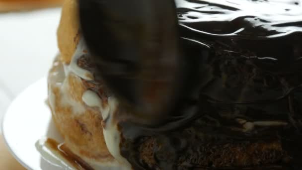 Vista de perto. Mulher espalhando um esmalte de hocolate em um bolo de esponja. Mão feminina derramar creme com uma colher no bolo e começar a se espalhar em um biscoito de laranja ou massa de bolo de esponja na cozinha — Vídeo de Stock