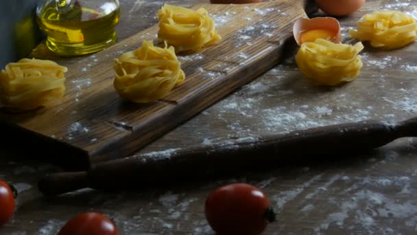 Тальятелле или паста феттучини гнездится на деревянной кухонной доске рядом со сломанным яичным желтком, помидорами черри, мукой и оливковым маслом в деревенском стиле. Итальянская кухня — стоковое видео