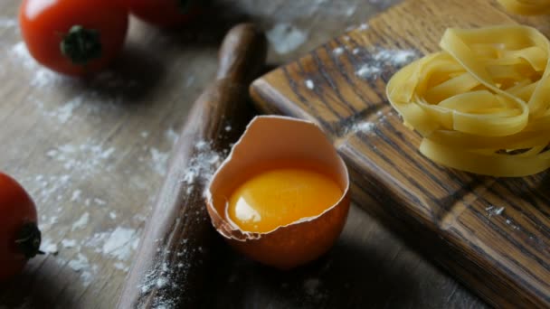 Fila de comida italiana nacional. Produtos de farinha crua vista de perto. Tagliatelle ou fettuccine massas ninhos em uma placa de cozinha de madeira ao lado de uma gema de ovo quebrada em um estilo rústico . — Vídeo de Stock