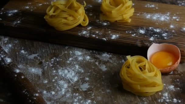 Italiano rolou massa fettuccine fresco. O espaguete Tagliatelle nidifica em uma placa de cozinha de madeira ao lado de uma gema de ovo quebrada, farinha e azeite em um estilo rústico. Alimentos nacionais italianos — Vídeo de Stock