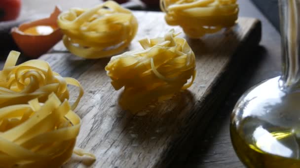 Las pastas de tagliatelle o fettuccine anidan en una tabla de cocina de madera junto a una yema de huevo rota, tomates cherry, harina y aceite de oliva en un estilo rústico. Comida nacional italiana — Vídeos de Stock