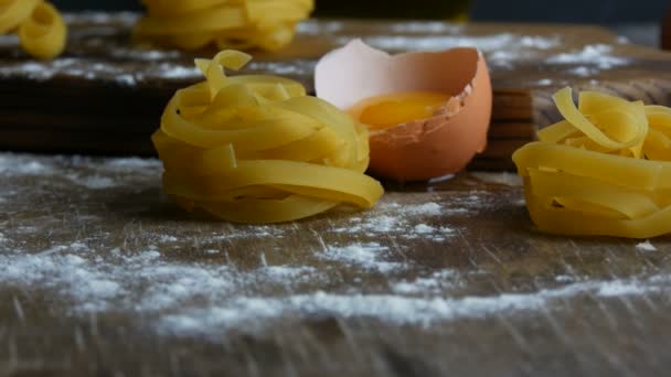 Close-up zicht op Italiaanse gerolde verse fettuccine pasta. Spaghetti Tagliatelle nestelt zich op een houten keukenbord naast een gebroken eigeel, bloem en olijfolie in een rustieke stijl. Nationaal Italiaans voedsel — Stockvideo