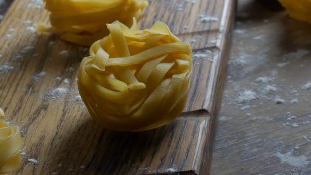 Vista de perto de italiano rolou massa fettuccine fresco. Esparguete Tagliatelle ninhos em uma placa de cozinha de madeira em estilo rústico. Alimentos nacionais italianos — Vídeo de Stock