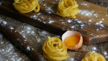 İtalyan usulü taze fettucine makarna. Spagetti Tagliatelle, kırık yumurta sarısı, un ve zeytinyağının yanında, ahşap mutfak tahtasına yuva yapar. Ulusal İtalyan yemekleri.