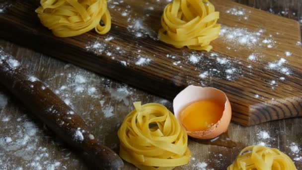 Ιταλικά τυλιγμένα φρέσκα ζυμαρικά φετουτσίνι. Σπαγγέτι Tagliatelle φωλιάζει σε ένα ξύλινο πίνακα κουζίνας δίπλα σε ένα σπασμένο κρόκο αυγού, αλεύρι και ελαιόλαδο σε ρουστίκ στυλ. Εθνικό ιταλικό φαγητό — Αρχείο Βίντεο